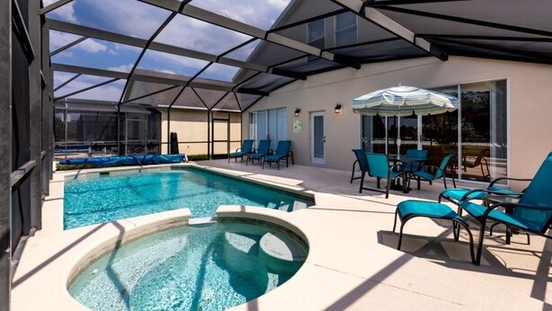 A pool area with a hot tub, lounge chairs, and a covered patio with a glass enclosure.