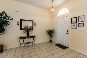 A hallway with a tiled floor, a white door, a console table with a mirror, and framed certificates on the wall. - 5BR Pool Home in Glenbrook by SHV-1907 (Clermont)