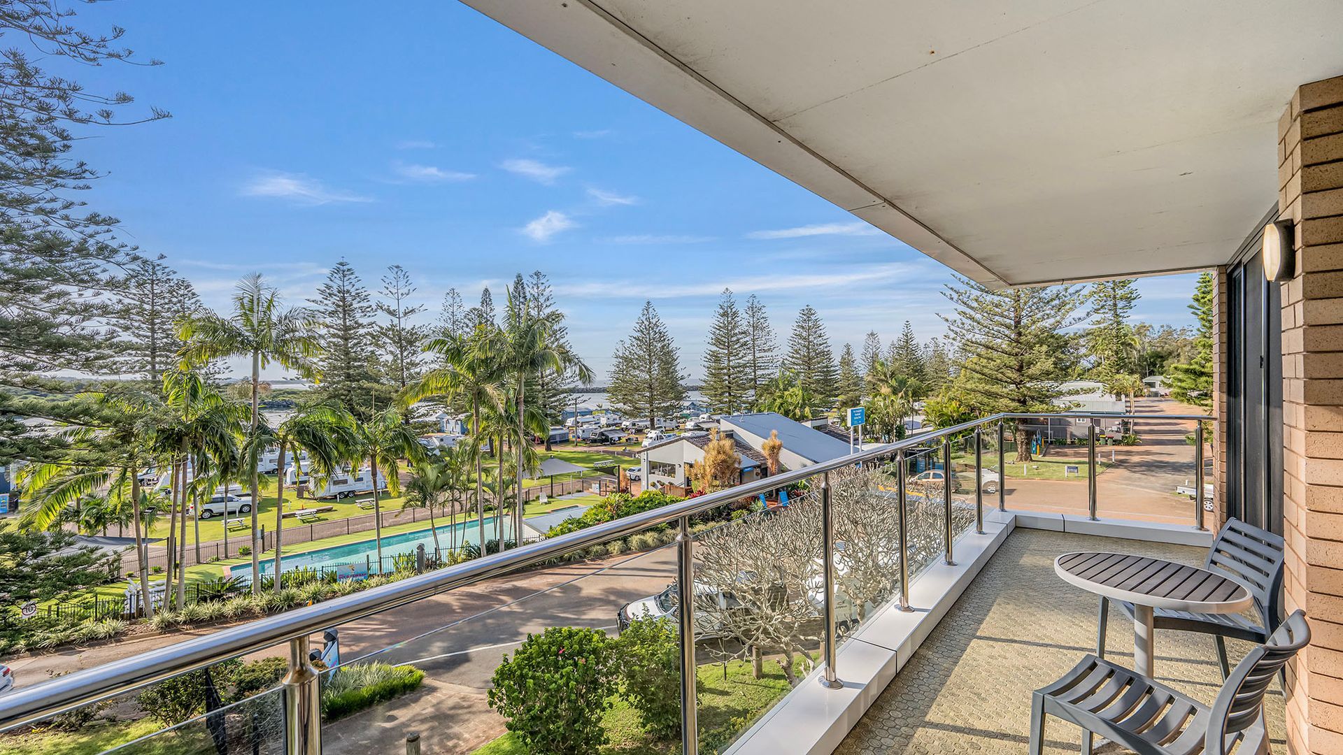 A balcony with a view of a pool, palm trees, and a parking area.