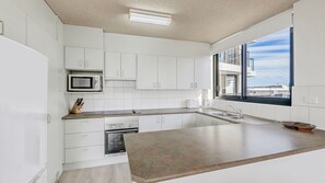 A modern kitchen with white cabinetry, a built-in microwave, and a large window offering a view of the city.