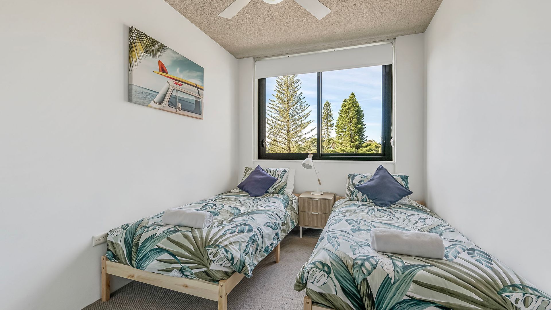 A bedroom with two single beds, a window with a view of trees, and a painting on the wall.