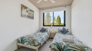 A bedroom with two single beds, a window with a view of trees, and a painting on the wall.