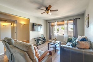Ein Wohnzimmer mit Deckenventilator, Flachbildfernseher, Glastisch und einer Couch mit Kissen.