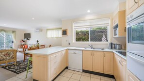 A compact kitchen with a dishwasher, a sink, and a stove. There's a dining area with a table and chairs, and a window with a view of greenery.