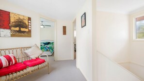 A hallway with a wicker sofa, a bed with a floral bedspread, and a ceiling fan.