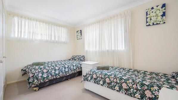 A bedroom with two single beds, a bedside table, and a window with sheer curtains.
