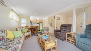 A living room with a sofa, armchairs, a coffee table, and a dining area with chairs and a table. - 3/54 Owen Street, Port Macquarie (Port Macquarie)