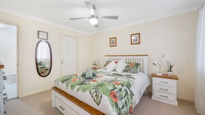 A bedroom with a bed, a ceiling fan, a bedside table with a lamp, a mirror, and a door. - 3/54 Owen Street, Port Macquarie (Port Macquarie)