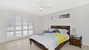 A bedroom with a bed, nightstands, a ceiling fan, and large windows with blinds. - Dolphins 2, 7 Commodore Crescent (Port Macquarie)