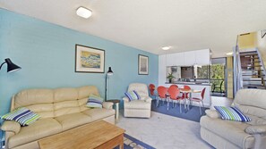 A living room with a sofa, armchairs, a coffee table, and a dining area with chairs and a table.