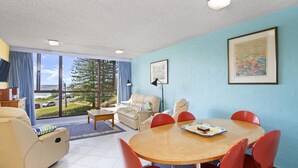 A room with a large window, a round table with chairs, a sofa, and a lamp. - Beachpark 56, 58 Pacific Drive (Port Macquarie)