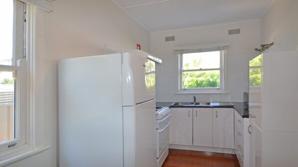 A small kitchen with white cabinets, a white refrigerator, a stove, and a window providing natural light.