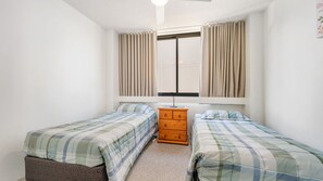 A bedroom with two beds, a dresser, and a window with curtains.