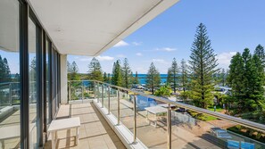 A balcony with a glass railing overlooking a parking area and a view of trees and a body of water. - Tasman Towers 12, 3 Munster Street (Port Macquarie)