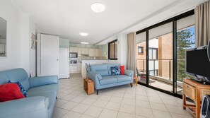 A modern apartment with a living room, kitchenette, and a balcony with a TV. - Tasman Towers 12, 3 Munster Street (Port Macquarie)