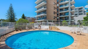 A swimming pool with a white fence, lounge chairs, and a multi-story building in the background. - Tasman Towers 12, 3 Munster Street (Port Macquarie)