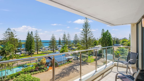 A balcony with a view of a pool, trees, and a distant body of water.