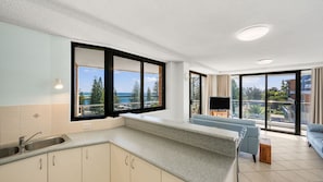 A modern kitchen with a large window, a built-in TV, and a balcony with a view of the sea.