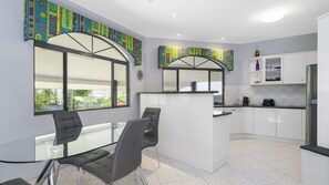 A modern kitchen with a central island, white cabinetry, and a large window providing a view of greenery.