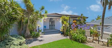 A residential property with a well-maintained lawn, a variety of tropical plants, and a modern house with solar panels.