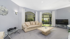 A modern living room with a beige sofa, a glass coffee table, and a flat-screen TV.