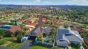 A residential area with houses, some with solar panels, surrounded by greenery and a clear sky.