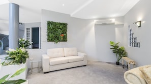 A modern living room with a white sofa, a glass coffee table, and a vertical garden wall.
