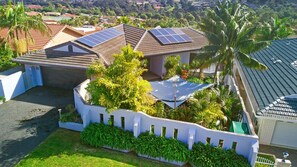 A residential property with solar panels on the roof, a white fence, and lush greenery.