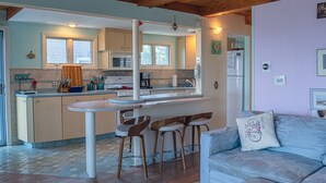 Una cocina moderna con una isla central, taburetes de bar y un sofá de color claro en un espacio habitable acogedor.
