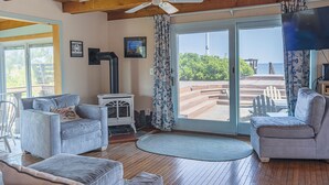 Una sala de estar acogedora con ventilador de techo, chimenea y un gran ventanal corredizo que da a una terraza con vista al océano.