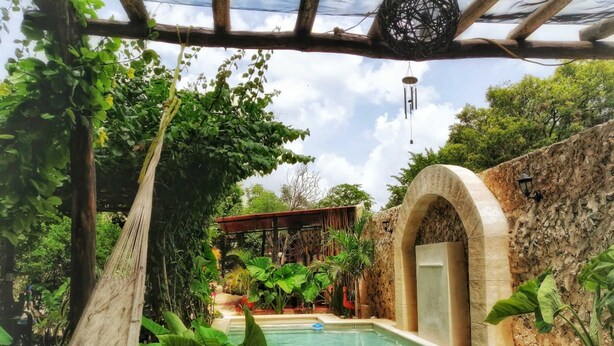 A pool area with a stone wall, a pergola, and lush greenery. - Casa Daniels (Valladolid)