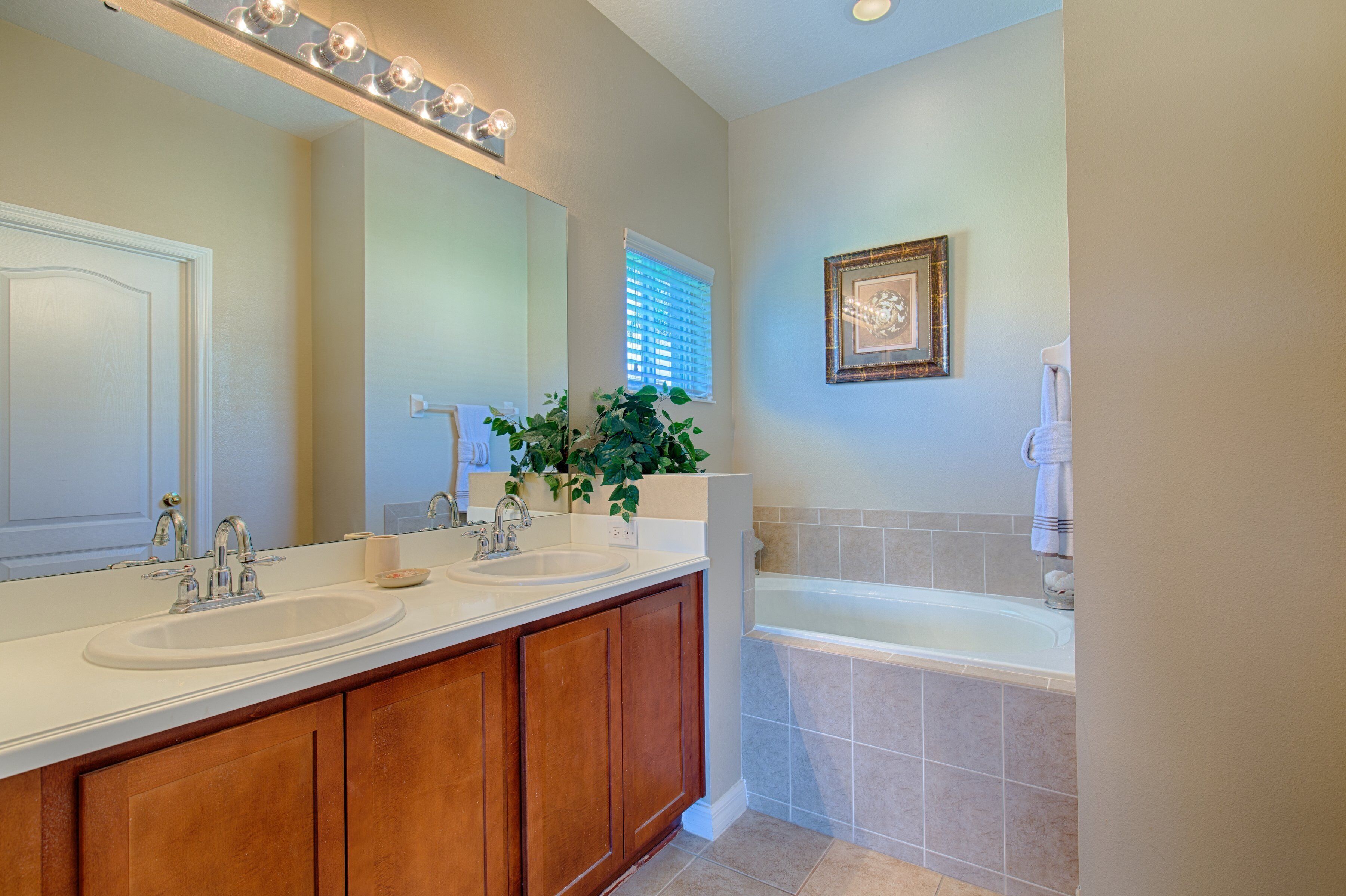A bathroom with a double sink vanity, a large mirror, and a bathtub.