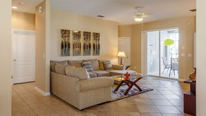 A living room with a beige sofa, a glass coffee table, and a painting on the wall. - 4-Bedroom Villa with Private Pool & Spa - near Disney & ChamionsGate (Davenport)