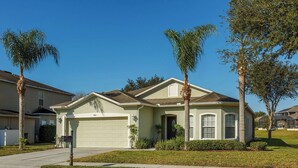 A single-story house with a garage, surrounded by well-maintained lawns and palm trees. - 4-Bedroom Villa with Private Pool & Spa - near Disney & ChamionsGate (Davenport)