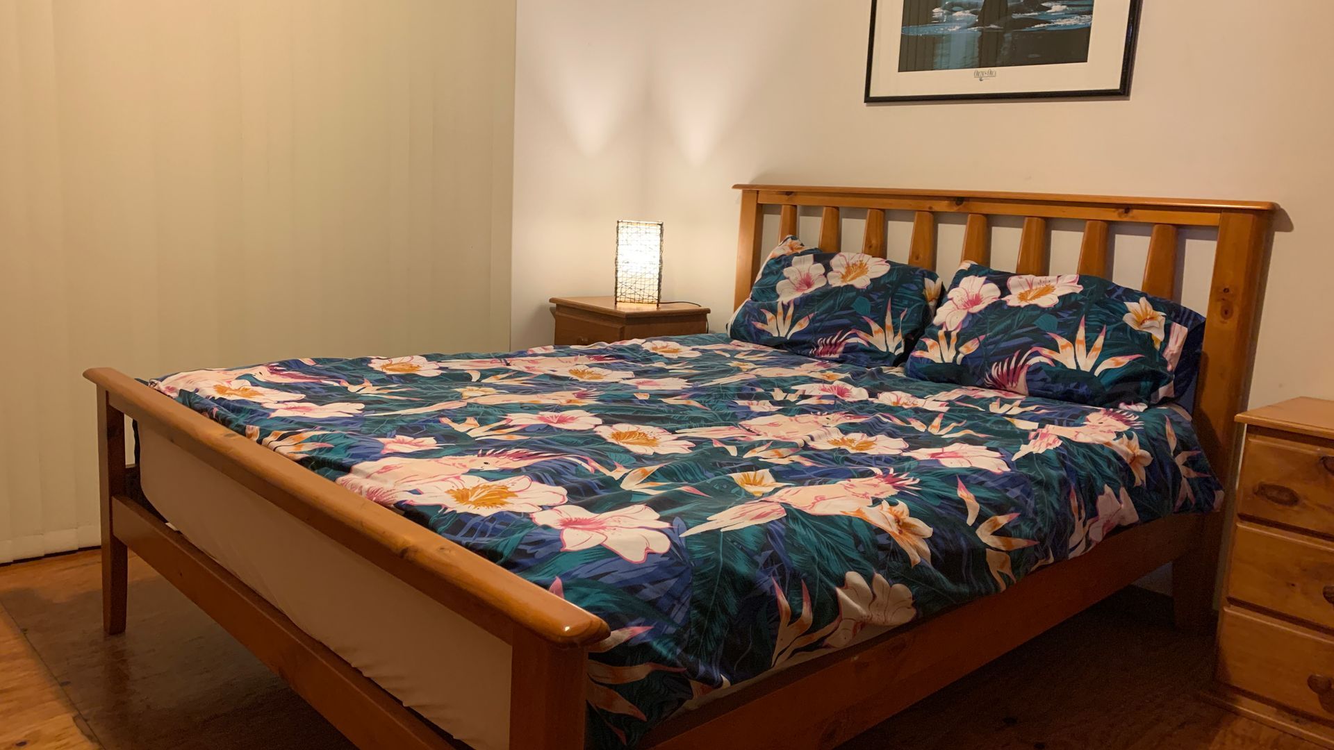 A bed with a floral bedspread, a nightstand with a lamp, and a framed picture on the wall.
