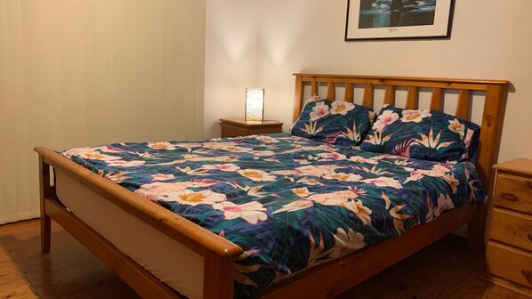 A bed with a floral bedspread, a nightstand with a lamp, and a framed picture on the wall. - Rocky Beach Cottage, 26 Pacific Drive (Port Macquarie)