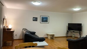A living room with a sofa, a small table, a television, and two framed pictures on the wall. - Rocky Beach Cottage, 26 Pacific Drive (Port Macquarie)