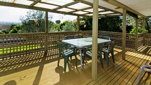 Alpendre coberto com mesa e cadeiras, rodeado por um deck de madeira e um painel de treliça.