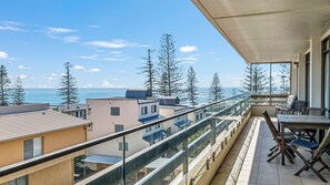 Un balcone con vista sul mare e sugli edifici, dotato di ringhiera in vetro e mobili da esterno.