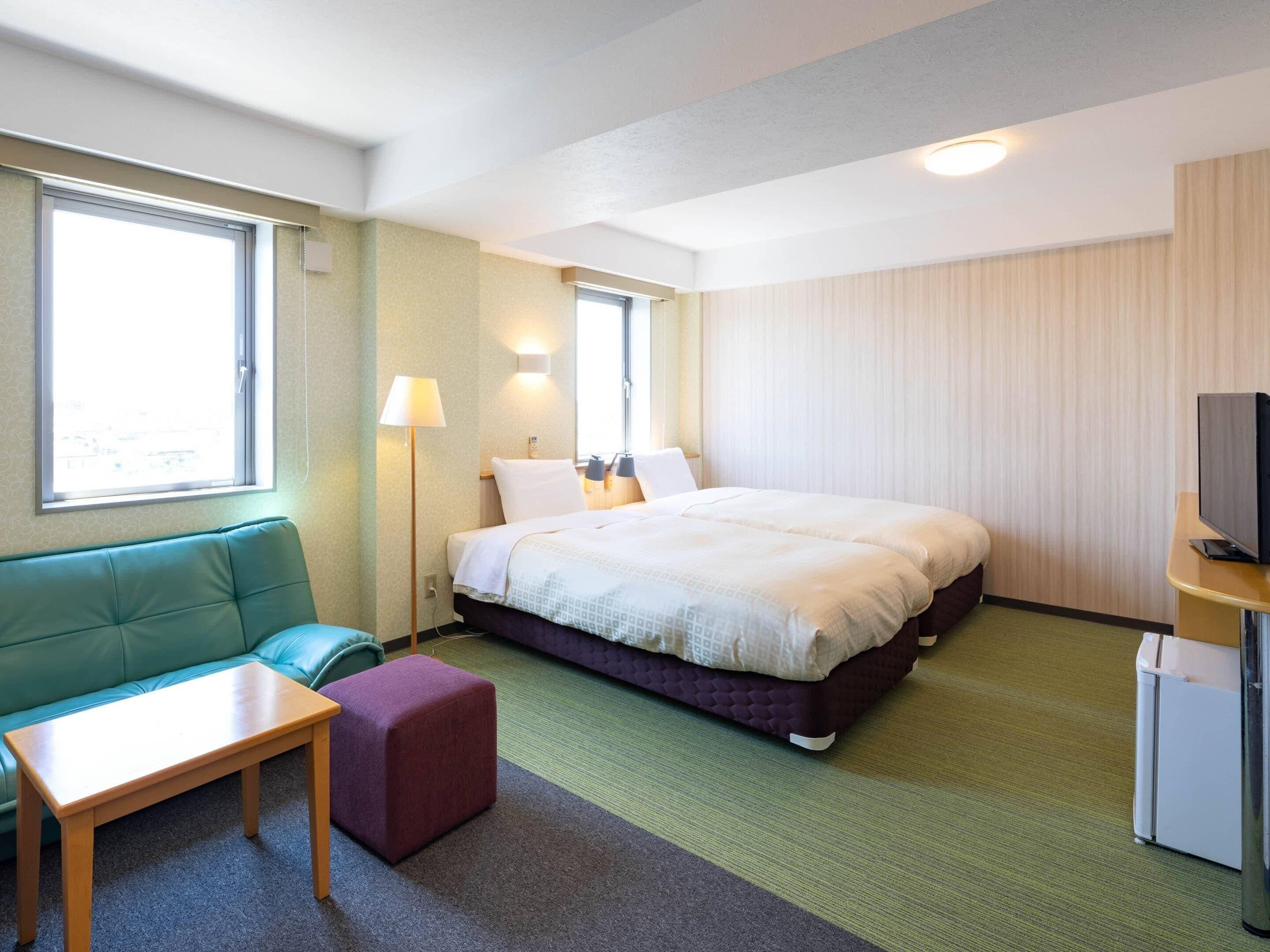 A hotel room with a bed, a sofa, a table, a TV, and a window.