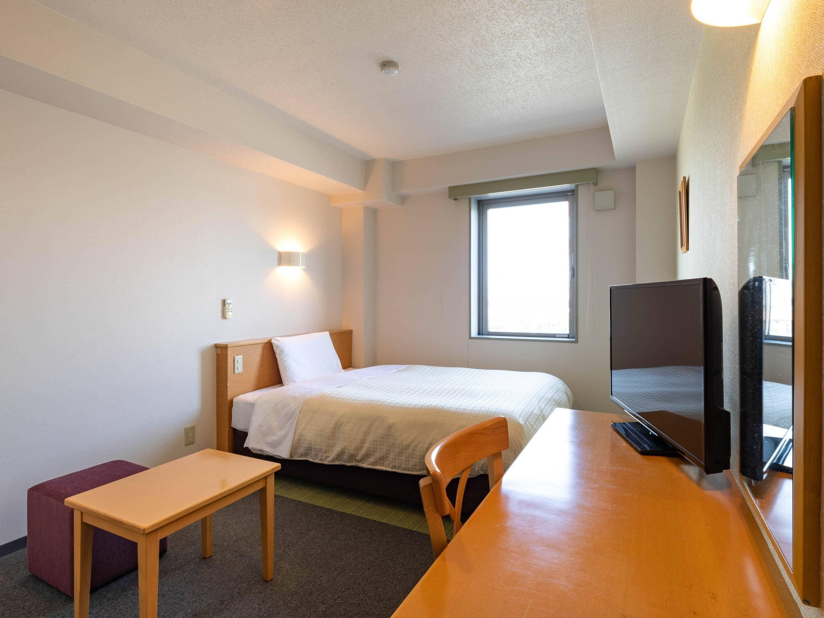 Una habitación de hotel con cama, escritorio, silla, televisor y ventana.