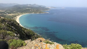 A coastal landscape with a clear view of the sea, a sandy beach, and surrounding hills.