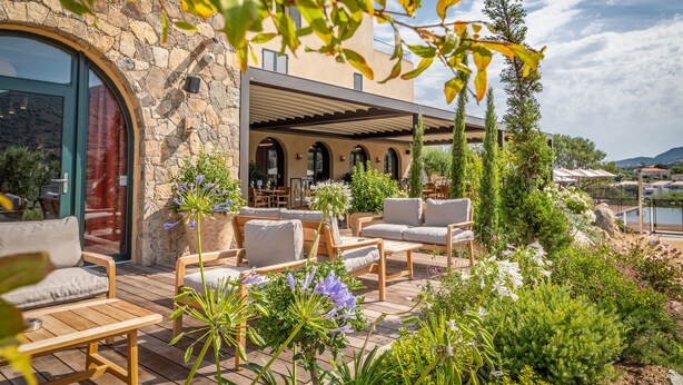 A patio area with outdoor seating, a stone wall, and a view of a body of water.