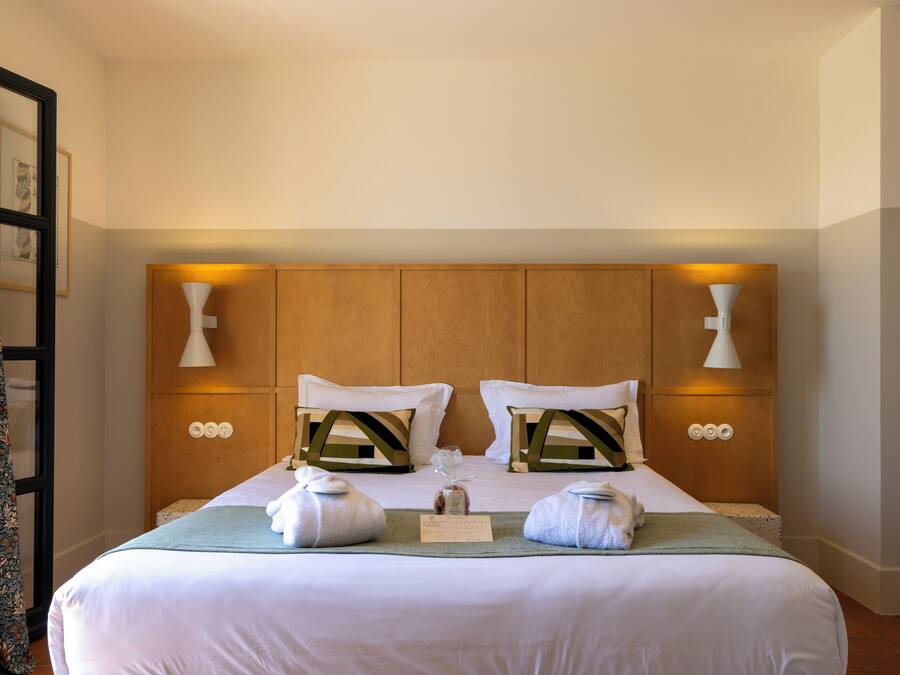 Una cama bien hecha con dos almohadas, una mesita de noche y una lámpara de pared.
