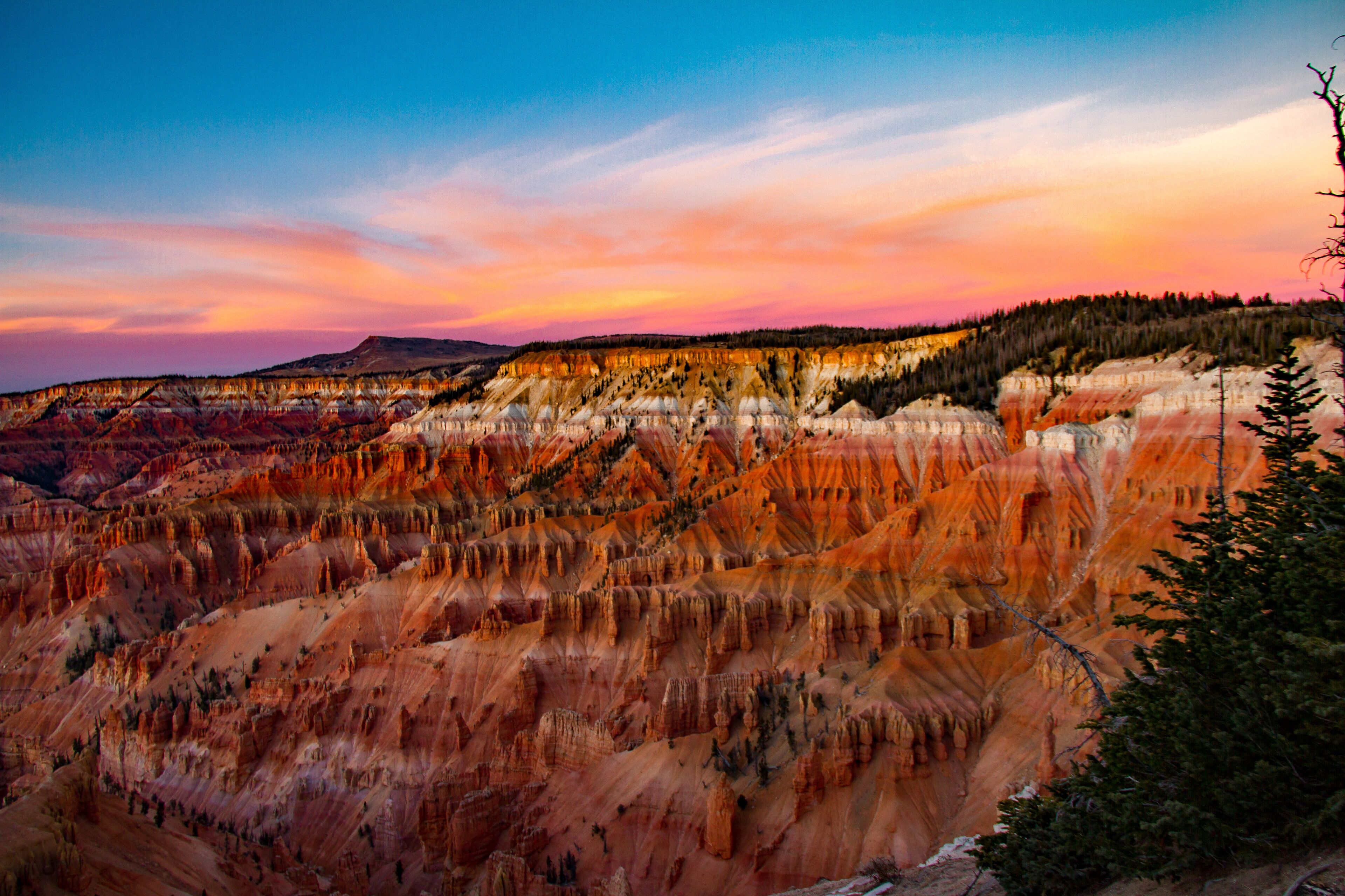 A panoramic view of a rugged landscape with layered rock formations and a forested hill in the distance.