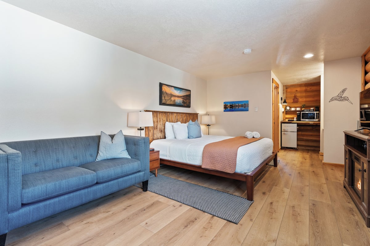 Une chambre à coucher avec un lit, un canapé bleu, un plancher en bois et, au fond, une petite cuisine.