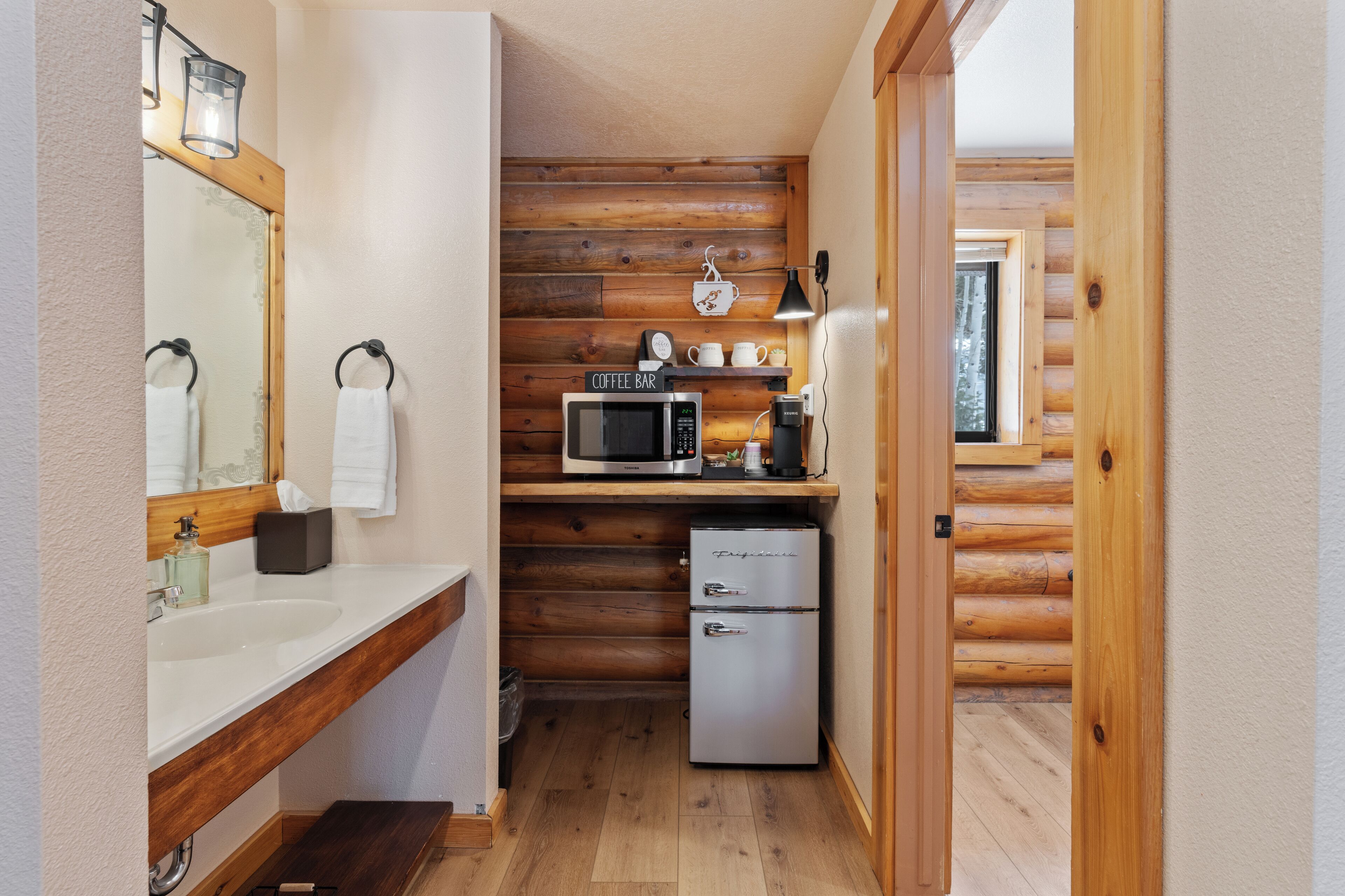 A compact kitchen with wooden walls, a microwave, a coffee maker, and a refrigerator.