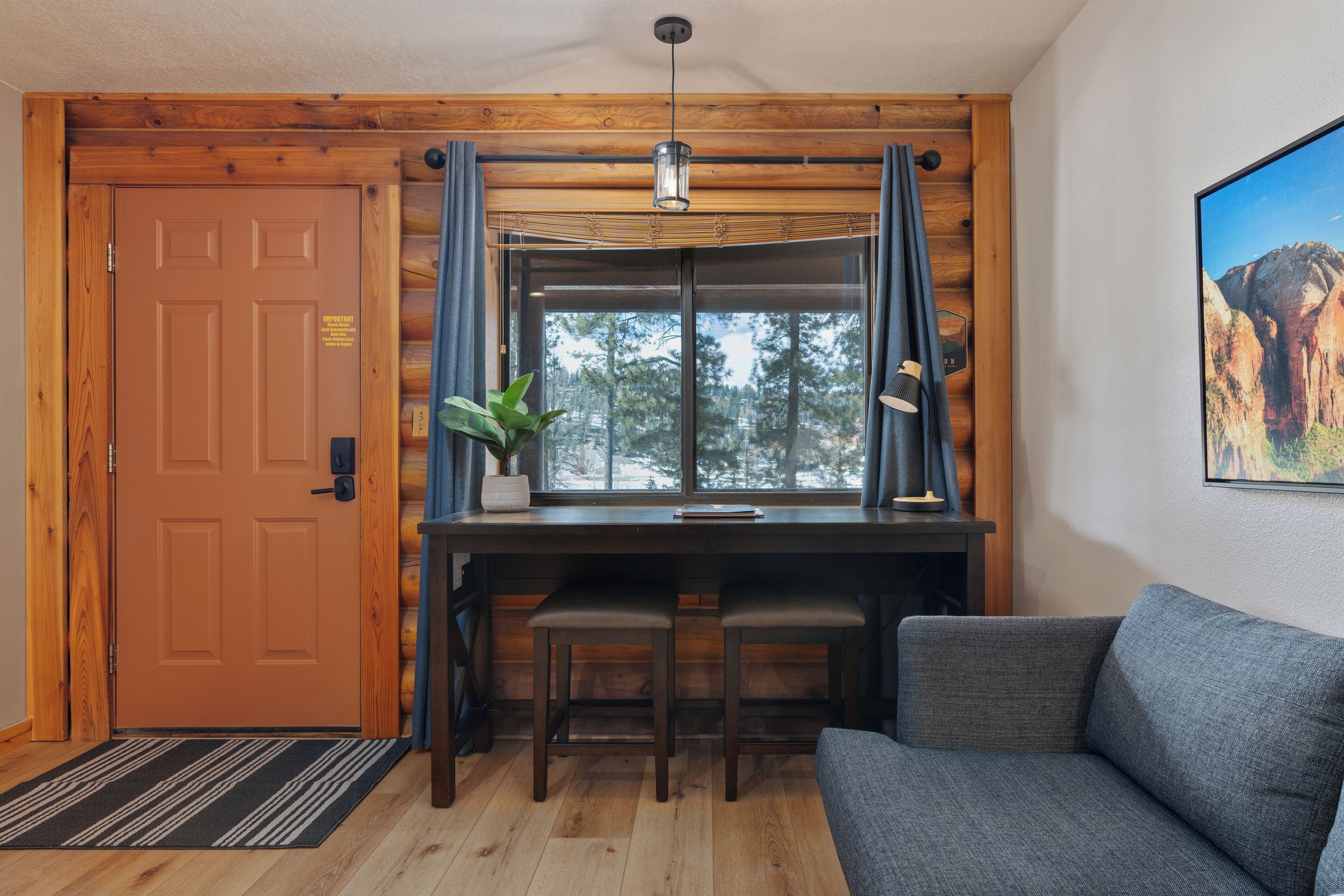 Un interior de madera con un escritorio, dos sillas, un sofá, una ventana con cortinas y una puerta.