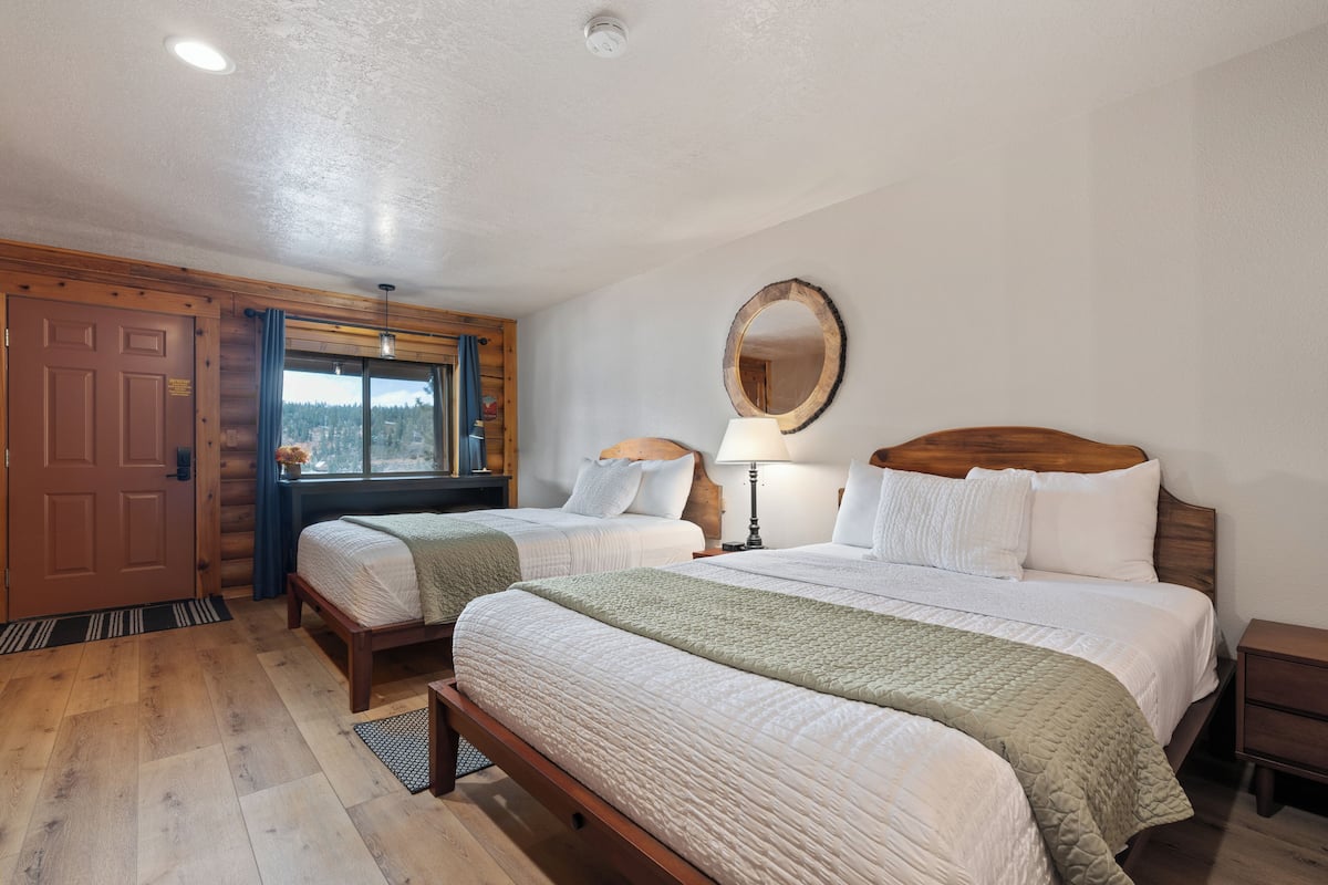 Une chambre avec deux lits, des têtes de lit en bois, un grand miroir et une fenêtre donnant sur un beau paysage.