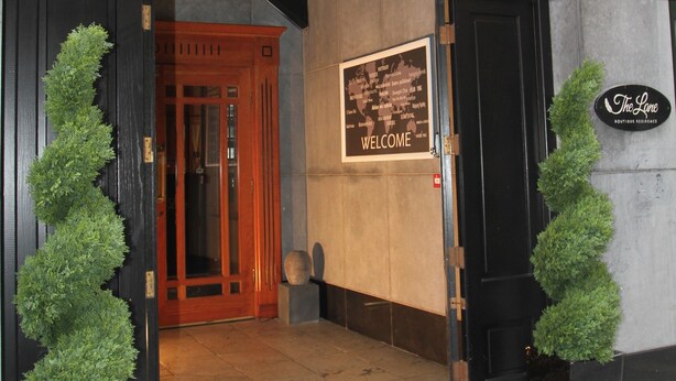 The Lane Boutique Hotel entrance with a dark wooden door, a welcome sign, and two potted plants on either side. - The Lane - Boutique Residence (Galway)